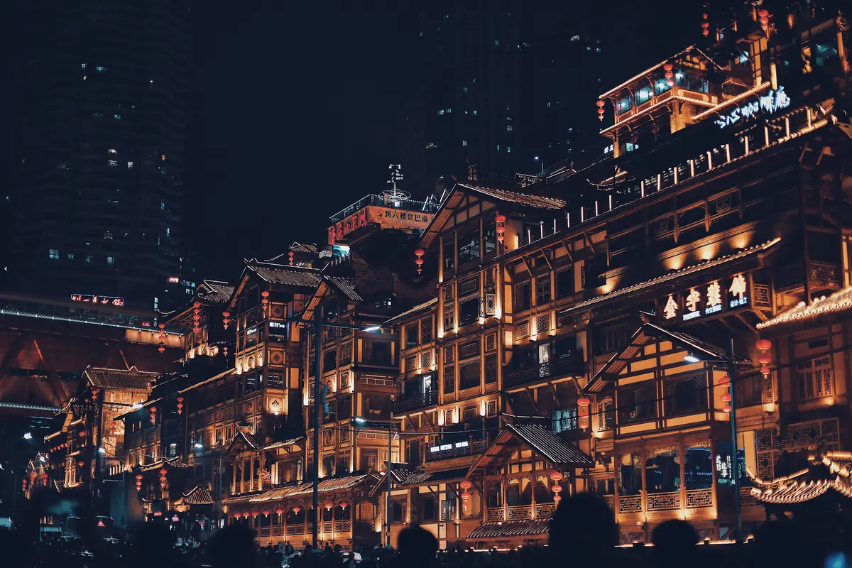 Rows of timber-fronted buildings in the stilt style glowing in warm light at dusk in Chongqing.