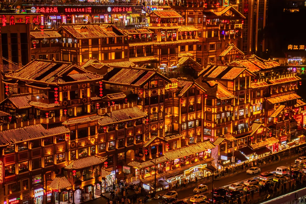 Tiers of golden-lit eaves and red lanterns on Chongqing's stilt-style riverfront at night.
