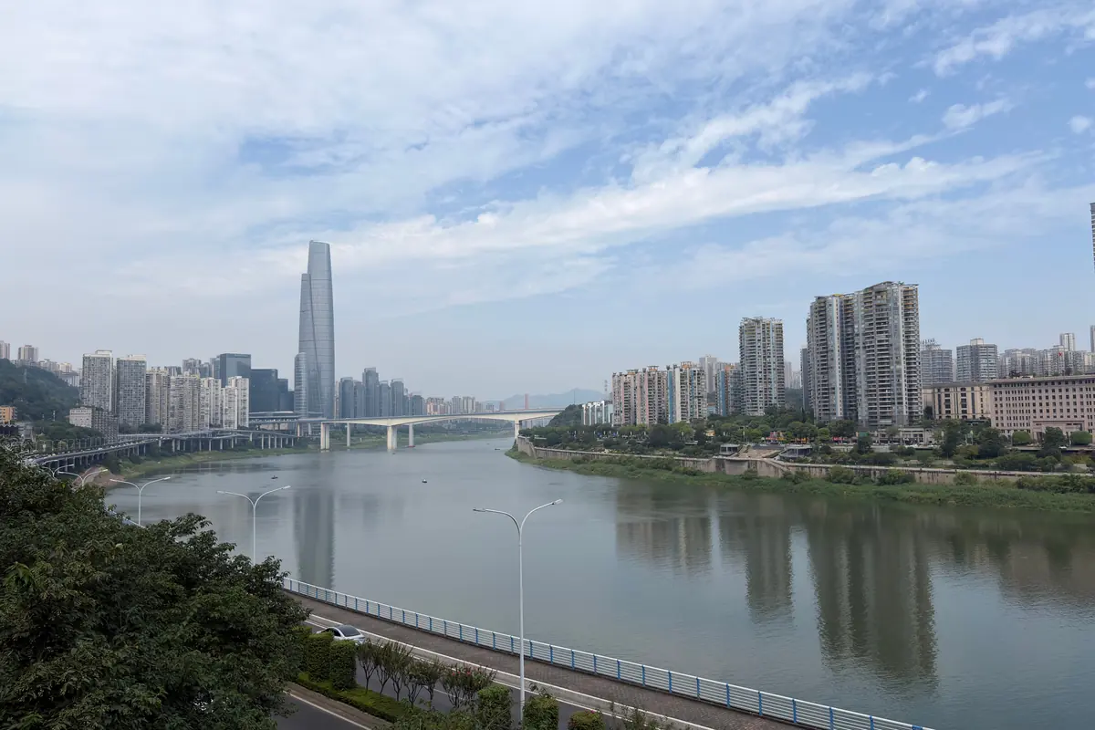 The Jialing River in daylight beside Chongqing's riverside roads, with a tall tower in the distance.