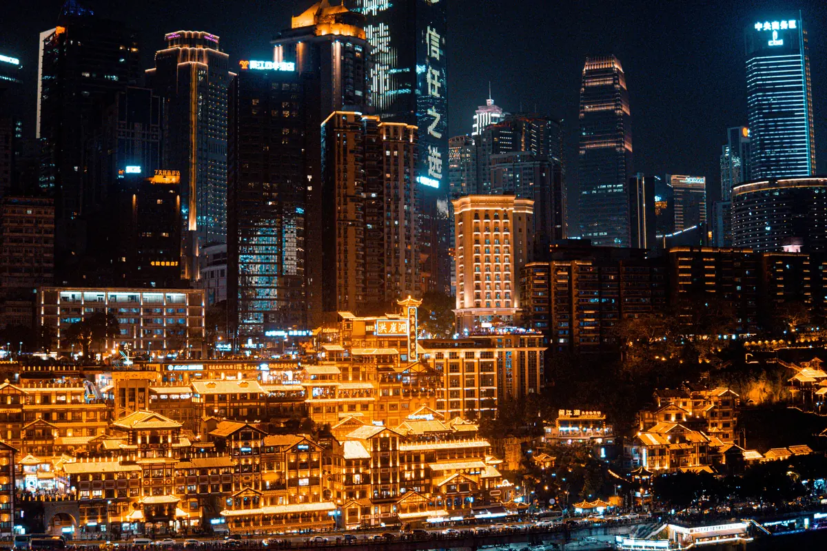 Hongya Cave's gold-lit terraces below the glass towers of Chongqing's city centre at night.